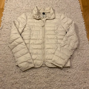 Vit pufferjacka från Only - Säljer en stilren vit pufferjacka från Only med quiltad design och dragkedja framtill. Jackan har hög krage, lång ärm och är tillverkad i lätt polyester. Perfekt för kyliga dagar när du vill hålla värmen och ändå se fräsch ut.