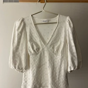 Vit blus med puffärm från Kappahl - Superfin vit blus från Kappahl med broderat hålmönster och v-ringning. Blusen har puffiga trekvartsärmar med resår vid ärmslut och en feminin passform. Perfekt för dig som gillar romantiska detaljer och stilren look.