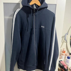 Hugo Boss zip up hoodie / luvtröja med dragkedja / kofta - Jätte fin Hugo boss zip up hoodie Mörkblå färg med vita och gråa detaljer I mycket bra skick Storlek XL på lappen, passar L bättre Skicka meddelande vid några funderingar  Kolla gärna även in mina andra annonser