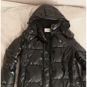 Glansig pufferjacka  - Svart pufferjacka från Calvin Klein med glansig finish. Perfekt för kalla dagar. Jackan är i storlek M  men skulle säga att den är lite mindre i storlek. Köpt på Zalando för 2200, bara hör av dig vid intresse 
