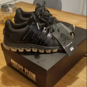  Philipp Plein skor - Säljer ett par svarta Philipp Plein sneakers med chunky transparent sula och coola detaljer på sidan. Skorna har snörning och branding både på sidan och hälen. Materialet är en mix av syntet och textil, perfekt för dig som gillar streetstyle. Helt nya köpt för 3500kr från Johnells 