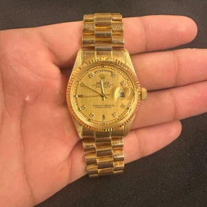 Klocka Day-Date  - Day-Date herrklocka i helguld med klassisk rund boett och länkarmband. Urtavlan är guldtonad med diamanter som timmarkeringar och har både dag- och datumvisning.   Perfekt för dig som gillar lyxig stil. Behöver nya batterier fungerar ej just nu. Har 3-extra länkar som kommer med 