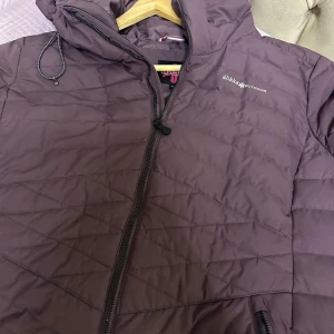 Mörkbrun pufferjacka från Åhkká - Säljer en mörkbrun pufferjacka från Åhkká Outdoor med huva och snygga quiltade detaljer. Jackan har dragkedja framtill och långa ärmar. Perfekt för kalla dagar och har en clean, sportig look. Fodret är gjort i syntetmaterial och jackan är riktigt lätt att bära.