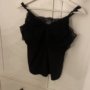 Svart spetslinne från Pieces XL - Säljer ett svart linne från Pieces i storlek XL men passar i storlek S oxå. Toppen har tunna justerbara axelband och vacker spets upptill som ger en snygg och feminin look. Materialet är mjukt och lätt, perfekt för att styla med jeans eller kjol. Spetsen har fina detaljer och ger linnet extra edge.