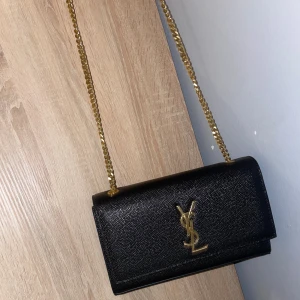 Svart Kate axelväska från Saint Laurent - Säljer en svart Kate axelväska från Saint Laurent med guldigt YSL-logo framtill och kedjerem. Tagit hand om den som min bebis. Den är i nyskick kan tänka mig gå ner lite vid snabbaffär.