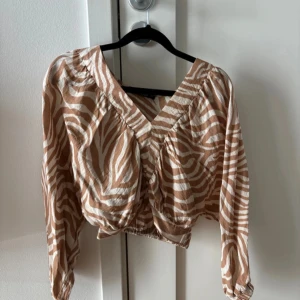 Zebramönstrad blus med v-ringning - Säljer en beige och vit zebramönstrad blus från Gina Tricot. Blusen har v-ringning och långa ärmar 