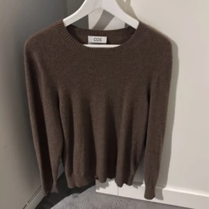 Brun kashmirtröja från COS - Superskön brun kashmirtröja från COS med rund hals och ribbade muddar vid ärmslut och nederkant. Perfekt för dig som gillar stilrena och mjuka plagg. Långärmad och i normal passform, passar till allt och är riktigt chill.