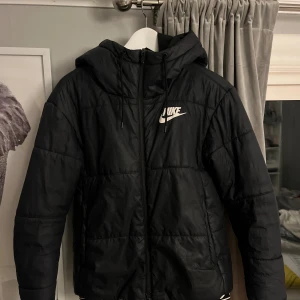 Svart pufferjacka från Nike  - Svart pufferjacka från Nike med vit logga på bröstet. Jackan har tyvärr blivit för liten för mig! Finns ett litet hål på ens ärmen, annars i bra skick!😁