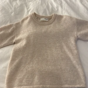 Beige stickad tröja från Selected Femme - Supermjuk och stilren beige stickad tröja från Selected Femme. Tröjan har korta ärmar, rund halsringning och en enkel, clean look. Perfekt för lager-på-lager och passar till allt. Snygg och enkel att matcha med jeans eller kjol.