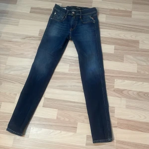 Replay Anbass slim jeans blå - Snygga mörkblå Replay Anbass jeans i slim fit med klassiska fem fickor och kontrastsömmar. Jeansen har en smal passform och är tillverkade i stretchigt denim för extra komfort. Perfekta för dig som gillar en modern och stilren look. Köpta för 1800, vid snabbaffär kan priset diskuteras!