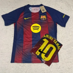 FC Barcelona Lamine Yamal #10 Nike tröja - Snygg FC Barcelona matchtröja med Lamine Yamal och nummer 10 på ryggen. Tröjan är kortärmad, har klassiska blå och röda vertikala ränder, gula detaljer och klubbmärke på bröstet. Tillverkad i lätt polyester med tryckta sponsorer och namn.