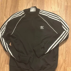 Svart Adidas track jacket med vita ränder - Längd: 65cm Bredd: 43cm