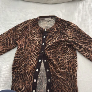 Leopardmönstrad kofta från Karen Millen - Snygg leopardmönstrad kofta från Karen Millen i bruna och svarta toner. Koftan har trekvarts ärmar, rund halsringning och silverfärgade knappar framtill. Perfekt för dig som vill sticka ut med ett djurmönster. Materialet känns mjukt och stretchigt.
