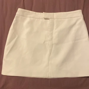 Vit kortkjol från Gina Tricot - Snygg vit kortkjol från Gina Tricot i klassisk rak modell. Kjolen har en stilren look med dold dragkedja framtill. Passar både S/M och L