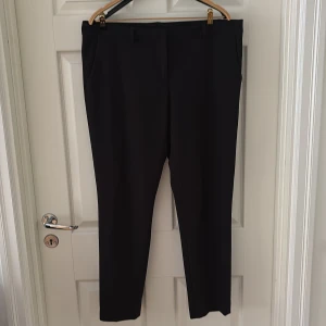 Svarta kostymbyxor  - Snygga svarta kostymbyxor med klassisk rak passform och diskreta fickor i sidorna. Byxorna har hällor för bälte och är perfekta för en stilren look. Materialet känns mjukt och följsamt, vilket gör dem bekväma att bära hela dagen.