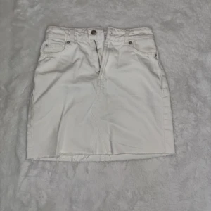 Vit jeanskjol med rå kant - Snygg vit jeanskjol med fem fickor och rå, fransig kant nertill. Klassisk knapp- och dragkedjestängning framtill. Perfekt för dig som gillar en enkel men trendig stil.