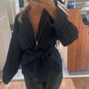 Mörkblå jeansjacka från Carin Wester - Snygg mörkblå jeansjacka från Carin Wester med breda ärmar, stora fickor och knytbälte i midjan. Jackan har dragkedja framtill + knappar.