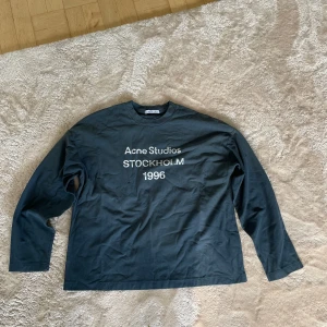 Navy blå långärmad tröja Acne Studios - Svart långärmad tröja från Acne Studios med tryck 'Acne Studios STOCKHOLM 1996' på bröstet. Tröjan har en klassisk rund halsringning och är gjord i mjuk bomull. Perfekt för en clean och stilren look. ny pris 3500