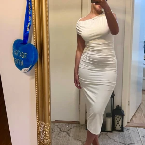 Vit oneshoulder långklänning - Säljer en elegant vit långklänning med oneshoulder-design och draperade detaljer längs sidorna. Klänningen har en tight passform som framhäver figuren och är tillverkad i ett mjukt, stretchigt material. Perfekt för dig som vill sticka ut med en stilren look.