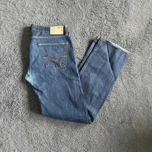 Replay Jennon jeans - Säljer ett par klassiska blå jeans från Replay med raka ben och snygga detaljer på bakfickorna. Jeansen har normal passform och är tillverkade i slitstarkt denim med en mörkblå tvätt. Perfekta för dig som gillar en enkel och stilren look. Har lite slitningar längst ned på bakbenen. Längd 112cm midja 44cm