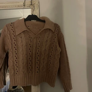 Beige stickad tröja med krage - Säljer en beige stickad tröja med  kabelstickat mönster och bred krage. Tröjan har v-ringning, långa ärmar och ribbade muddar. 