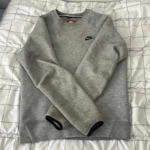 Grå Nike sweatshirt i bomull - Snygg grå sweatshirt från Nike med svart logga på bröstet. Tröjan har rund halsringning, långa ärmar och ribbade muddar. Perfekt för en chill och sportig stil. Tillverkad i mjuk bomullsmix som känns skön mot huden.