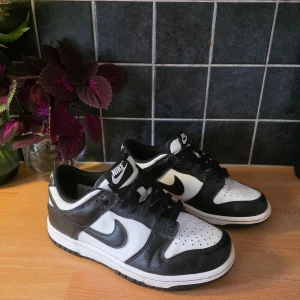 Nike Dunk Low svart/vit sneakers - Säljer ett par Nike Dunk Low sneakers i klassisk svart och vit färg. Skorna har svart swoosh, svarta snören och perforerad tåbox för extra ventilation. Tillverkade i skinn med låg profil och platt sula. Perfekta för dig som gillar streetstyle och vill ha en ikonisk look. Köpta för 1100kr. Pris går att diskutera 