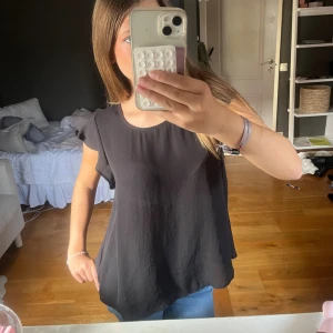 Svart blus från Gina Tricot - Säljer en svart blus från Gina Tricot i storlek 36. Blusen har rund halsringning, korta ärmar med lätt volang och är i ett tunt, flowy material som ger en snygg och avslappnad look. Perfekt att matcha med jeans eller kjol för en enkel stil. Jag har XS i strl och denna blir lite oversized på mig men fortfarande blir det fint. Passar S o M med!! Kanske L