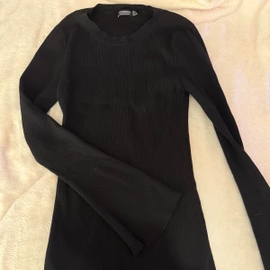Svart ribbad klänning från Stradivarius - Svart långärmad klänning från Stradivarius i storlek L. Klänningen är ribbad och har en rund halsringning. Perfekt basplagg med tight passform.