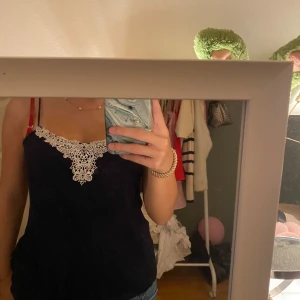 Mörkblå linnetopp med spetsdetalj - Säljer en mörkblå linnetopp med tunna axelband och snygg vit spetsdetalj framtill vid ringningen. Toppen har en avslappnad passform och är perfekt att styla med jeans eller kjol för en trendig look.