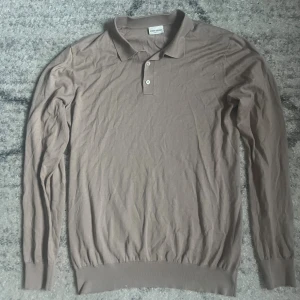 Beige långärmad pikétröja John Henric - Snygg beige långärmad pikétröja från John Henric med klassisk krage och två knappar framtill. Tröjan är tillverkad i mjuk bomull och har ribbade muddar vid ärmslut och nederkant. Perfekt för dig som gillar stilrena och enkla plagg.