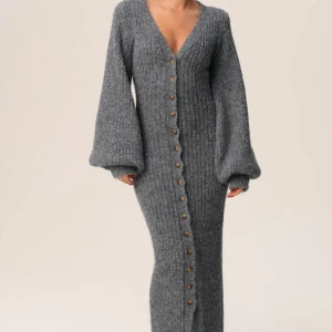 Adoore klänning  - Mysig långklänning i grå stickad kvalitet med v-ringning och stora ballongärmar. Klänningen har ribbad struktur och knappar hela vägen framtill, vilket ger en cool och avslappnad vibe. Perfekt för lager-på-lager och chill dagar.