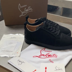 Christian Louboutin svarta sneakers mocka - Snygga svarta sneakers från Christian Louboutin i lyxig mocka med klassisk röd sula och diskret logga bak. Skorna har rund tå, svarta snören och en stilren design som passar perfekt till streetwear eller en mer uppklädd look.