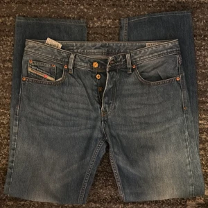 Blå Diesel jeans med raka ben - Snygga blå jeans från Diesel med klassisk femficksdesign, raka ben och coola detaljer som kopparfärgade nitar och knappar. Jeansen är tillverkade i 100% bomull och har en läderpatch med Diesel-logo bak i midjan. Perfekta för en avslappnad streetstil.
