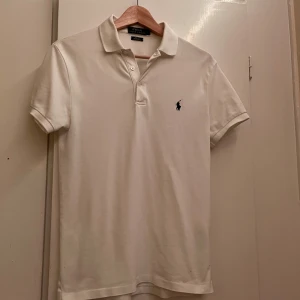 Ralph Lauren Piké - Vit pikétröja från Polo Ralph Lauren i slim fit med stretch mesh-material. Klassisk krage, korta ärmar och broderad logga på bröstet. Perfekt för en clean och stilren look.