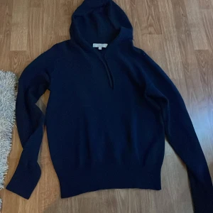 Mörkblå hoodie i kashmir från Carmés - Mysig mörkblå hoodie från Carmés i 100% kashmir. Tröjan har lång ärm, huva och klassisk passform. Perfekt för dig som gillar stilrena och bekväma plagg med exklusiv känsla. Enkel design utan tryck eller detaljer. Hör av dig vid frågor o funderingar