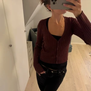 Vinröd ribbad kofta från Vero Moda - Säljer en vinröd ribbad kofta från Vero Moda i storlek M. Koftan har v-ringning, knappar framtill och är croppad i modellen. Långärmad och i mjukt, stretchigt material som sitter snyggt på kroppen. Perfekt att styla med jeans eller kjol.