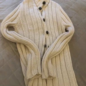 Beige stickad kofta från D&G - Säljer en chunky beige stickad kofta från Dolce & Gabbana. Koftan har grov ribbstickning, stora svarta knappar framtill och lång ärm. Perfekt för lager-på-lager och riktigt mysig till kyliga dagar.