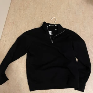 Svart half zip-tröja Jack & Jones - Svart långärmad tröja från Jack & Jones med half zip-dragkedja i halsen. Klassisk och enkel design med hög krage och mjukt material, perfekt för lager-på-lager. Passar dig som gillar stilrena plagg med en sportig touch.