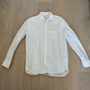 Vit prickig skjorta Oscar of Sweden - Snygg vit skjorta från Oscar of Sweden med små svarta prickar. Klassisk krage, långärmad och regular fit. Skjortan har bröstficka och knäppning framtill. Perfekt för dig som gillar stilrena detaljer och vill ha något som sticker ut lite. Storlek 42 och aldrig använd.