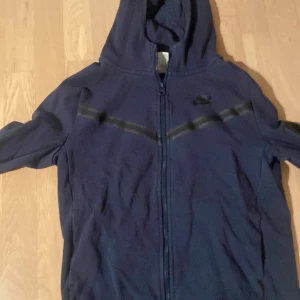 Mörkblå Nike mjukisbyxor med snörning - Mörkblå mjukisbyxor från Nike med elastisk midja och snörning. Byxorna har en avslappnad passform, sidofickor och diskret Nike-logga på låret. Perfekta för chill dagar eller träning. Mjukt material som känns skönt mot huden.