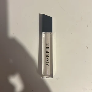 Morphe läppglans Issa Vibe - Glansigt läppglans från Morphe i nyansen Issa Vibe. Kommer i en stilren fyrkantig tub med svart lock och genomskinlig behållare som visar det skimrande, transparenta glanset. Perfekt för att ge läpparna en fräsch och glansig finish.