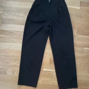 Svarta kostymbyxor från H&M - Svarta kostymbyxor från H&M med hög midja och raka ben. Byxorna har hällor för bälte, knapp och dragkedja framtill samt diskreta fickor bak. Ankellånga, perfekt för dig som är 155-160 cm! 💖 mått: midja, 31cm. Höfter: 48cm. Längd: 95cm  (hela)