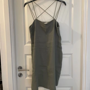Grön ribbad klänning från H&M - Snygg grön ribbad klänning från H&M med smala axelband som korsas i ryggen. Klänningen har en enkel och stilren design med en rak passform och ärmlös modell. Perfekt för dig som gillar minimalistisk stil och vill ha något bekvämt och trendigt.
