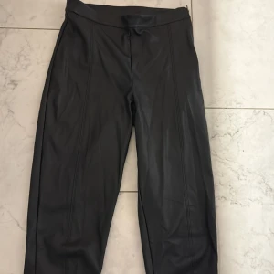 Svarta skinnbyxor från Gina Tricot XS - Snygga svarta skinnbyxor från Gina Tricot i storlek XS. Byxorna har en tight passform, hög midja och dragkedja i sidan. Materialet är mjukt och följsamt syntetskinn som ger en cool look. Ser helt oanvända ut och är väldigt sköna. Köparen står för frakt och paket skickas per post :)