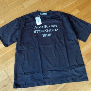 Svart t-shirt Acne Studios Stockholm - Svart t-shirt från Acne Studios med tryck 'Acne Studios STOCKHOLM 1996' på bröstet. Modellen är kortärmad och har en loose passform. Perfekt för dig som gillar stilrena och trendiga plagg med tydlig logga.