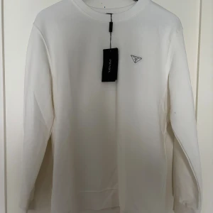 Vit sweatshirt från Prada - Säljer en stilren vit långärmad tröja från Prada med klassisk rund halsringning och diskret logotyp på bröstet. Tröjan är i mjuk bomull och har en clean look som passar perfekt till jeans eller dressade byxor.