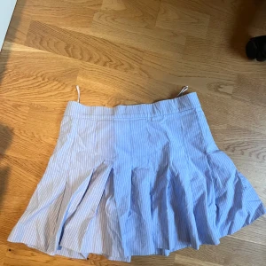 Blåvit randig kjol från Zara - Superfin blåvit randig kjol från Zara med plisserade detaljer och klassisk kort modell. Kjolen har en fräsch och somrig vibe, perfekt för dig som gillar preppy stil. Tillverkad i bomull för en skön och luftig känsla.