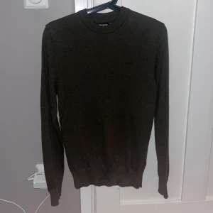 Mörkgrön stickad tröja J.Lindeberg - Snygg mörkgrön stickad tröja från J.Lindeberg med diskret logga på bröstet. Rund hals och ribbade muddar vid ärmslut och nederkant. Perfekt för dig som gillar stilrena och klassiska plagg med en modern touch. Nypris 1399kr använd max 3 gånger och rensar nu ur garderoben.