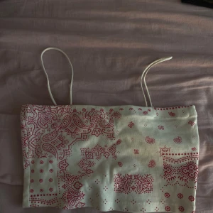 Vit och röd bandana-linnetopp XS - Säljer en vit linne-topp från XSIDE i storlek XS med tunna axelband och rött bandanamönster. Toppen har raka linjer och är perfekt för dig som gillar en trendig och avslappnad stil. Materialet känns mjukt och lätt mot huden.